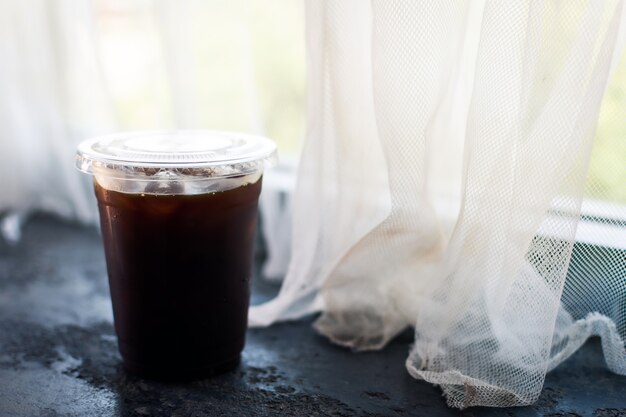 Americano-koffie in plastic beker bij het raam.