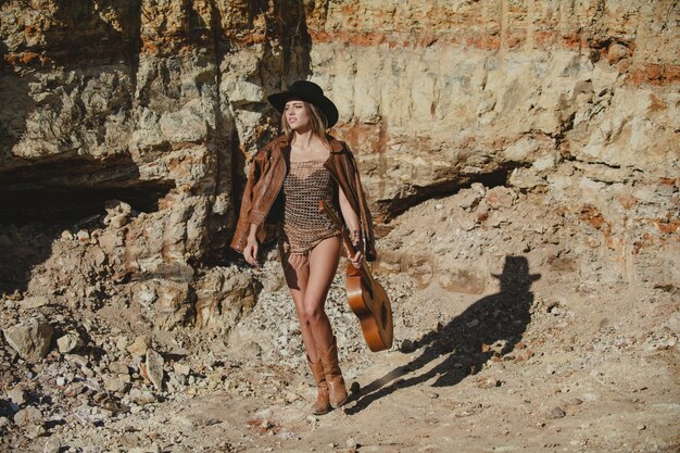 Amerikaans meisje met gitaar in fashion cowgirl cowboy-stijl Aantrekkelijke vrouw in fashion outfit buiten Outdoor fashion foto van jonge mooie dame die geniet van de lente