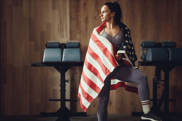 Amerikaans patriotmeisje met een atletische lichaamsbouw die zich voordeed op een houten muurachtergrond bedekt met een vlag van de vs.