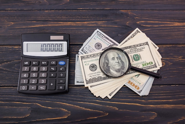 Amerikaanse dollars met een vergrootglas en rekenmachine op een houten achtergrond. Uitzicht van boven.