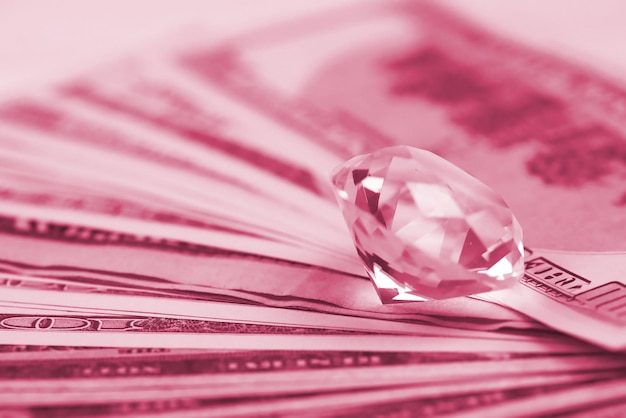 Amerikaanse geldbiljetten met grote diamant close-up Grote hoeveelheid dollars en enorme transparante edelsteen op tafel Zaken en juwelen Afbeelding afgezwakt in Viva Magenta kleur van het jaar 2023