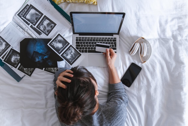 Amerikaanse jonge volwassen vrouw controleert medische resultaten met kaart in de hand laptop met wit scherm op het bed kopieer ruimte gezondheidszorg concept