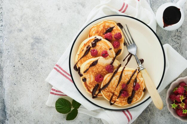 Amerikaanse pannenkoeken Pannenkoeken met verse frambozen met chocoladeglazuur of toppings in grijze kom op lichtgrijze tafelachtergrond Zelfgemaakte klassieke Amerikaanse pannenkoeken Pagina voor tijdschriftconcept Bovenaanzicht