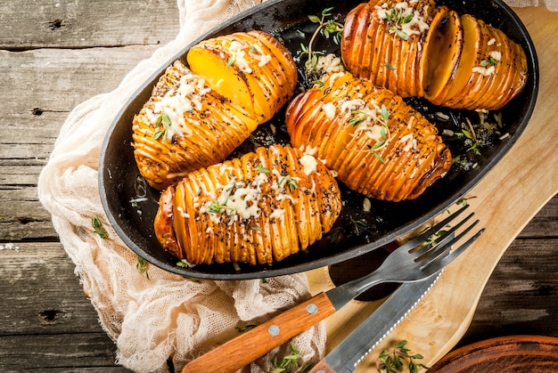 Amerikaanse traditionele huisgemaakte gerechten. het veganistische dieet. eigengemaakte hasselback-aardappel met verse kruiden en kaas. op oude houten tafel, kopie ruimte