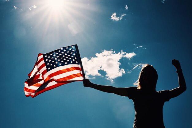 Foto amerikaanse vlag buitenshuis vrouw silhouet houdt usa nationale vlag tegen blauwe bewolkte hemel th juli onafhankelijkheidsdag