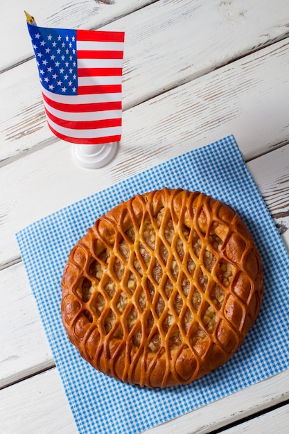 Amerikaanse vlag en ronde taart. Taart op servet naast vlag. Vers gebak op witte tafel. Traditionele taart met fruitvulling.