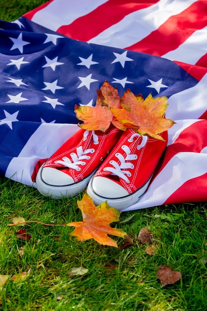 Amerikaanse vlag met esdoornbladeren en rode gumshoes op groen gras in de herfst