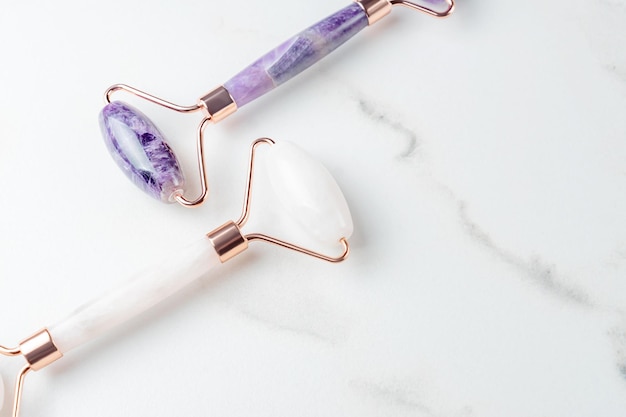 Photo amethyst and rose quartz massage rollers on marble background pink jade stone for face and body