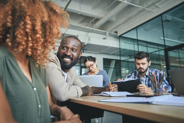 Photo amicable man smiling at young lady at conference meeting