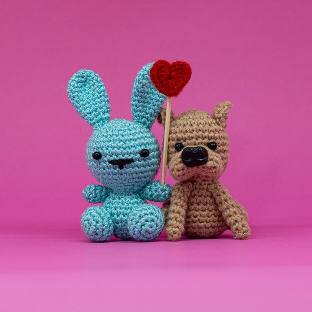 amigurumi of rabbit and dog with a heart, on pink background.