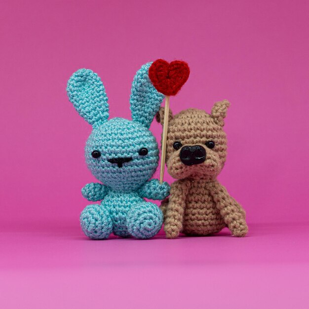 Amigurumi of rabbit and dog with a heart, on pink background.