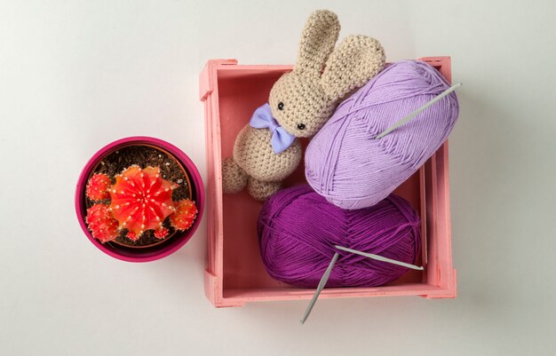 Amigurumi rabbit with black eyes and bow tie, cactus, wool box and crochet hooks