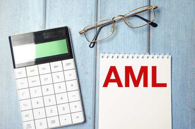 AML AntiMoney Laundering text on notepad and glasses calculator on wooden background