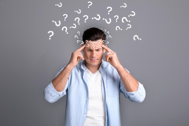 Amnesia concept man surrounded by question marks trying to remember something on grey background