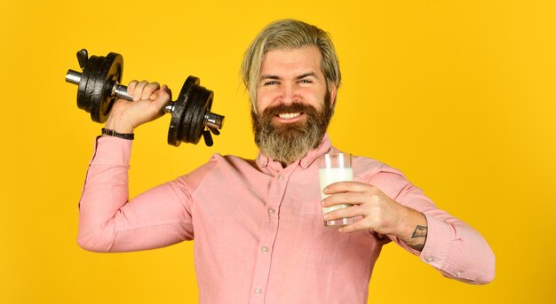 Amount of fat. Vitamins for muscles. Sportsman hold dumbbell and glass of milk. Protein diet. Protein cocktail. Source of calcium. Bearded man drink milk. Exercise in gym. Milk good nutrients.