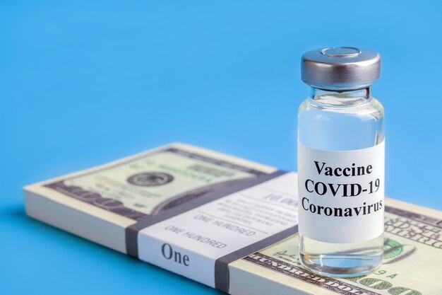 Ampoule with vaccine against the virus on pack of hundred-dollar bills on blue