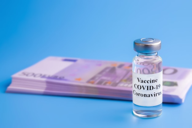 Ampoule with vaccine and packs of euro bills with syringe on blue