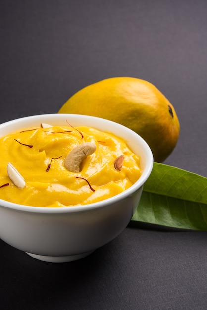 Foto amrakhand è uno yogurt al gusto di alphonso o shrikhand, popolare dolce indiano servito con frutta secca e zafferano con frutta intera di mango, su sfondo colorato. messa a fuoco selettiva