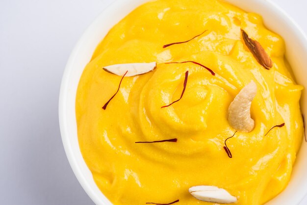 Amrakhand is an Alphonso flavoured Yogurt or Shrikhand, Popular Indian sweet served with dry fruits &amp; Saffron with whole mango fruit, over colourful background. selective focus