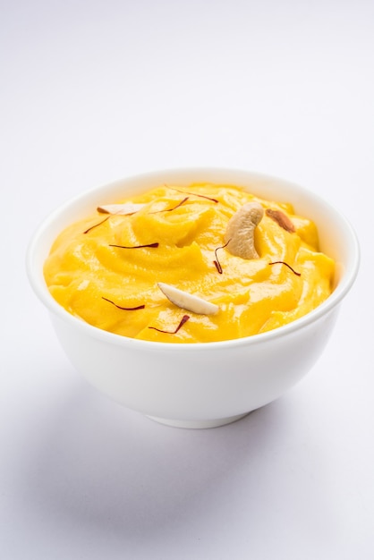Амракханд - это йогурт со вкусом Альфонсо или Шрикханд, популярная индийская сладость, которую подают с сухими фруктами и шафраном с цельными плодами манго на красочном фоне. выборочный фокус