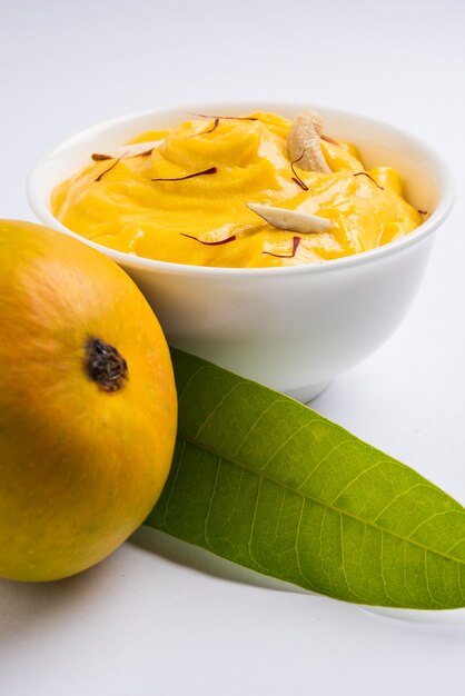 Amrakhand is een Alphonso gearomatiseerde yoghurt of Shrikhand, populair Indiaas snoepje geserveerd met droog fruit en saffraan met hele mangofruit, op een kleurrijke achtergrond. selectieve focus