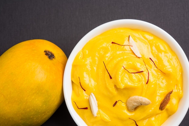 Amrakhand is een Alphonso gearomatiseerde yoghurt of Shrikhand, populair Indiaas snoepje geserveerd met droog fruit en saffraan met hele mangofruit, op een kleurrijke achtergrond. selectieve focus