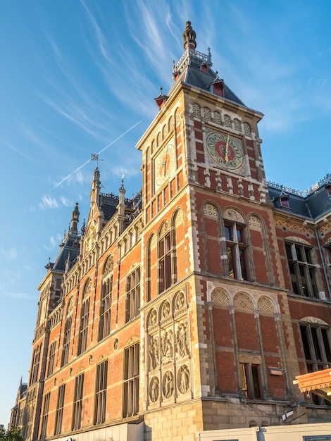 암스테르담 기차역 건물은 흐린 푸른 하늘 아래 오후 햇빛 아래 독특한 건축 디자인으로 탁월합니다.