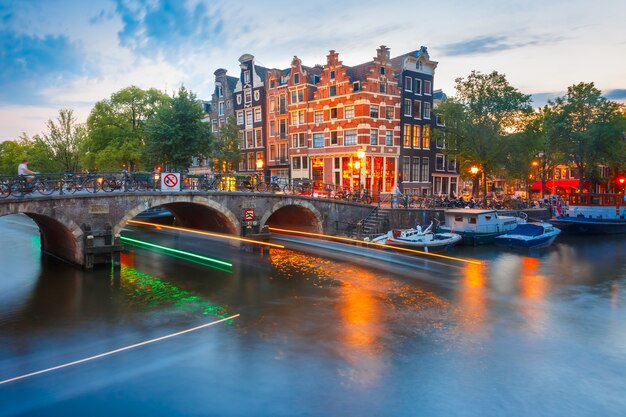 Amsterdamse gracht, brug en typische huizen, boten en lichtgevende baan vanaf de boot tijdens het ochtendschemering blauw uur, Holland, Nederland.