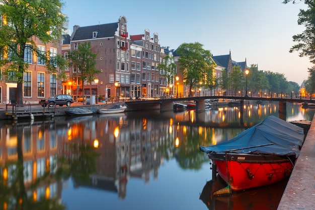 Amsterdamse gracht Kloveniersburgwal met typisch Nederlandse huizen, brug en woonboten tijdens ochtend blauw uur, Holland, Nederland.