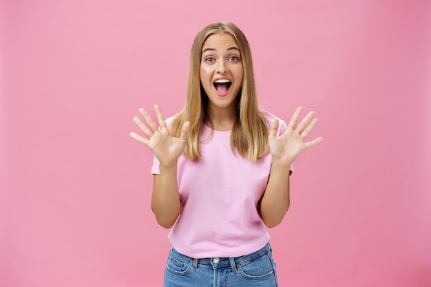 Photo amused and surprised excited attractive young caucasian female in casual t-shirt gesturing with spread fingers over chest smiling broadly with amazement looking  telling awesome news