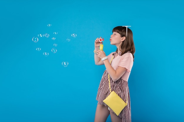 Amusing. Inspired lovely girl wearing stylish clothes and blowing soap bubbles