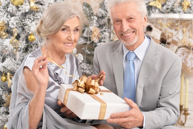 Amusing old couple with Christmas present near tree