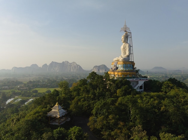 タイのバンコク近くのラーチャブリーにあるノンホイ寺院で、山の上に立つ大仏の空撮が際立っています。