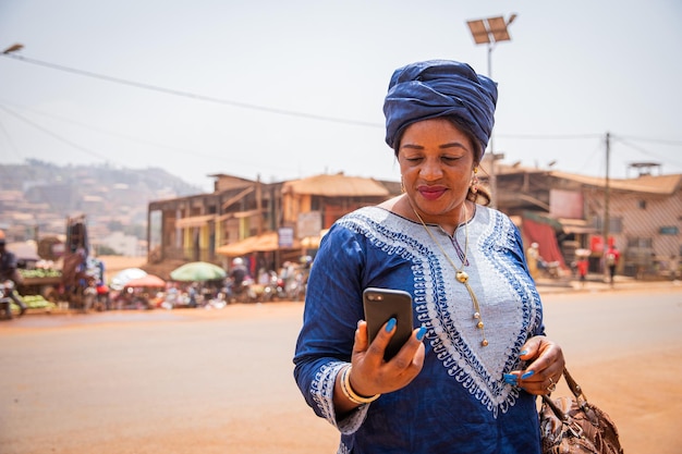 Фото Африканская женщина, одетая в традиционную одежду, смотрит на экран своего смартфона 50-летняя женщина из африканской деревни использует технику