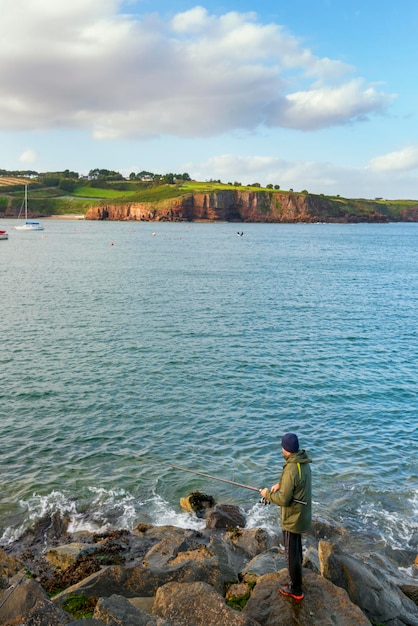 写真 アイルランドの海岸で美しい風景を背景に釣りをする釣り人