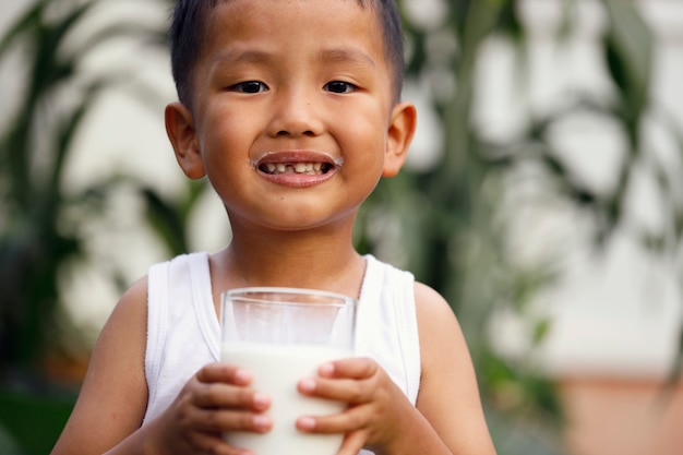 写真 アジアの少年が大きなグラスから牛乳を飲んでいます。
