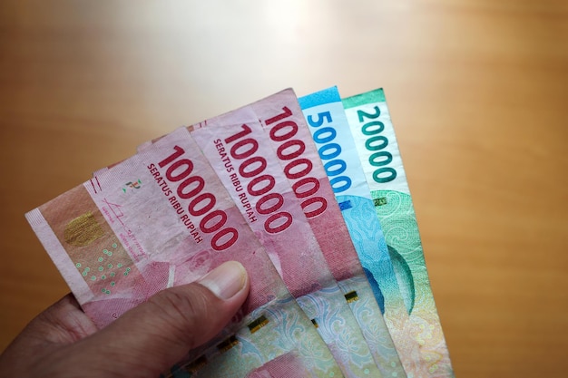 Фото Азиатский мужчина держит индонезийские деньги в поверхностном фокусе сбережения и дарения концепции