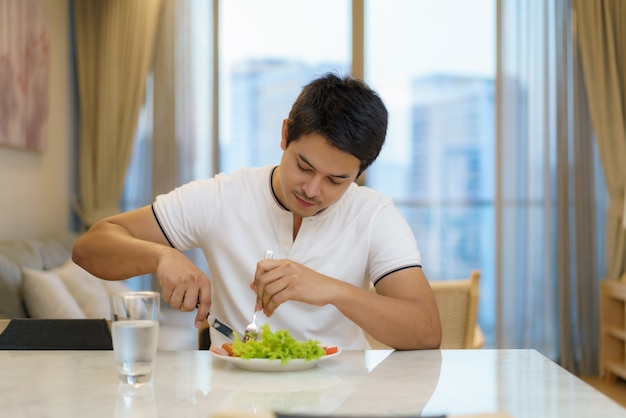 アジア人の男性が自宅の居間でアメリカンブレックファーストを食べています。