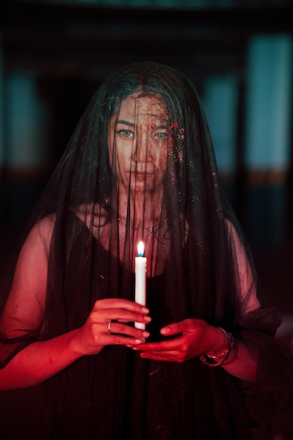사진 피로 뒤덮인 투명한 베일을 쓴 아시아 여성이 손에 촛불을 들고 있다