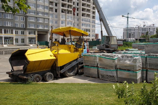 Фото На стройке припаркован асфальтоукладчик. дорожно-строительная техника стоит у дороги на складе. строительство тяжелых дорог и ремонт городских улиц.