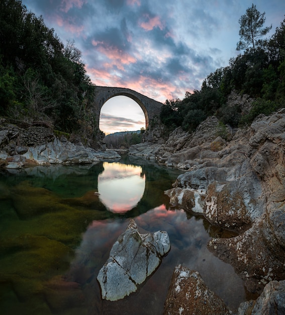 写真 岩とスペインの中世の橋の間の川の劇的な空の夕日の反射をマージする驚くべき風景