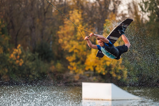 Фото Спортсмен делает трюк с трамплина гонщик прыгает на доске на фоне зеленого леса закат на озере