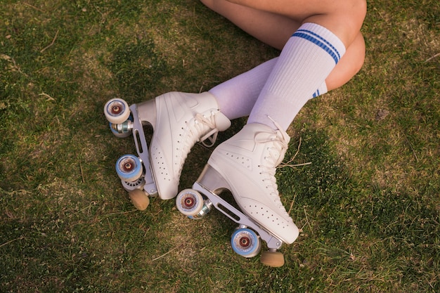 緑の芝生に横になっている白いビンテージローラースケートを着ている女性の足の上から見た図