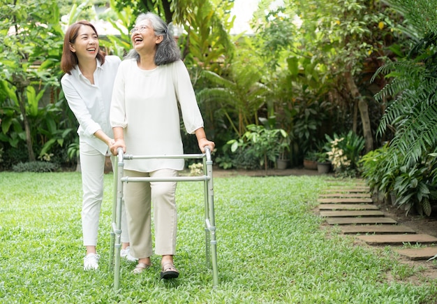 アジアの老婆が歩行器を使い、娘と一緒に裏庭を歩いている