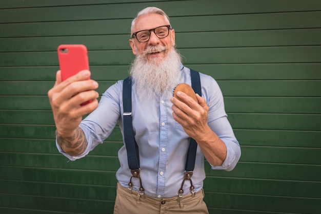 写真 流行に敏感な服と眼鏡をかけた年配の男性と長い白いあごひげが彼のあごひげをとかして写真を撮る