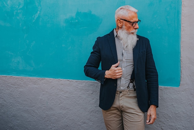 写真 流行に敏感な服と眼鏡をかけた年配の男性と長い白ひげが青い壁にポーズをとる