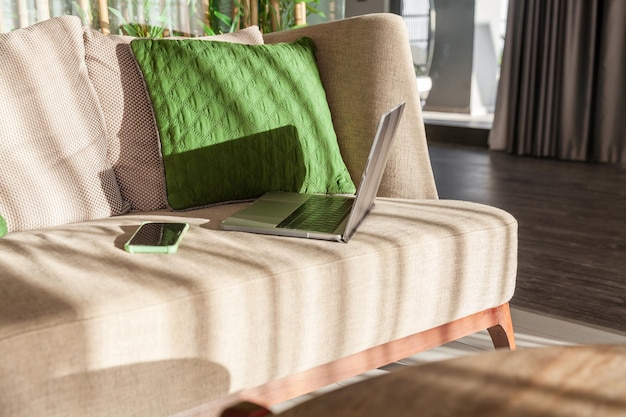 Фото Открытый ноутбук и телефон лежат на диване рядом с зеленой подушкой