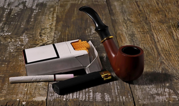 Фото Открытая пачка сигарет, зажигатель, сигарета и курильная трубка на грубом деревянном фоне.