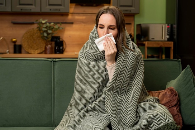Фото Несчастная расстроенная брюнетка сидит дома на зеленом диване страдает от простуды и использует