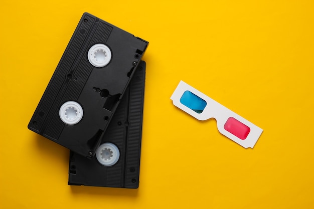 Photo anaglyph disposable paper 3d glasses and video cassette on yellow background. retro media, entertainment 80s. top view